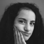 Mulher jovem tocando o rosto com a mão, representando cuidados com a pele e prevenção de linhas de expressão