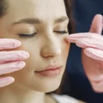Mulher com os olhos fechados durante tratamento facial com as mãos de uma profissional posicionadas sobre o rosto